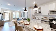 This single-story 2-bedroom, 2-bathroom residence combines modern design with functional living across a well-appointed floor plan. The open-concept kitchen serves as the heart of the home, featuring white shaker cabinetry, open shelving, granite countertops, stainless steel appliances, and a large island with pendant lighting that doubles as a casual dining area with bar seating. The kitchen flows seamlessly into the living room, which is bathed in natural light from large windows and a glass door that opens to an outdoor area, creating a bright and welcoming atmosphere with warm wood-style flooring throughout. The primary bedroom offers a generous footprint with plush carpeting, natural light from dual windows, and access to a well-organized walk-in closet featuring multi-tier shelving. The second bedroom is equally comfortable, with soft carpeting and warm ambient lighting. Both bathrooms are finished with granite-topped vanities and white cabinetry; one includes a soaking tub with subway tile surround. A dedicated hallway leads to the primary bath, providing added privacy. Two closets throughout the unit offer practical storage solutions, completing this efficiently designed and stylishly finished residence.