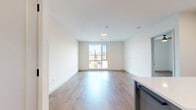 This well-appointed two-bedroom, two-bathroom residence in Boston, MA offers a thoughtfully designed single-floor layout with modern finishes throughout. The open-concept kitchen and living area serves as the heart of the home, featuring white upper cabinetry, two-tone lower cabinetry in navy and gray, a white quartz countertop island on casters, a white subway tile backsplash, and a full suite of stainless steel appliances. Warm hardwood flooring flows seamlessly through the kitchen, living, and bedroom areas, creating a cohesive and inviting atmosphere. Both bedrooms are generously proportioned, each offering large picture windows that frame views of the Boston cityscape and fill the rooms with abundant natural light. Ceiling fans add comfort, while clean white walls provide a bright, neutral backdrop. A dedicated walk-in closet with wire shelving provides ample storage. The two bathrooms are finished with large-format neutral tile flooring, floating wood-toned vanities, white quartz countertops, rectangular mirrors, and matte black hardware accents. One bathroom features a glass-enclosed walk-in shower with vertical white tile. The overall aesthetic is clean, contemporary, and move-in ready.