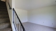 This two-floor space offers a straightforward and functional layout designed to maximize usability across both levels. The interior is finished with neutral white walls throughout, creating a clean and bright atmosphere that feels open and versatile. Soft, speckled wall-to-wall carpeting covers the floors, adding warmth and comfort underfoot. A staircase with dark metal railings serves as the central connection between the two floors, providing a sleek contrast against the lighter surroundings. The upper level opens into a spacious, open room bathed in natural light, with ample wall outlets suggesting flexibility for a variety of uses. The high, smooth ceilings contribute to an airy feel, enhancing the sense of space. The minimalist design of the interiors provides a blank canvas, making it easy to adapt each area to specific needs — whether residential or otherwise. Overall, the space presents a clean, uncluttered environment with practical finishes and a calm, neutral ambiance throughout.