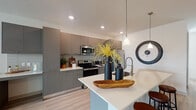 This two-floor residence showcases a cohesive modern design with light-toned hardwood-style flooring and a neutral color palette that flows throughout the main living areas. The kitchen is a standout feature, equipped with stainless steel appliances including a French door refrigerator, electric range, and built-in microwave. Flat-front cabinetry in a warm taupe finish lines the walls, complemented by white quartz countertops and a spacious waterfall island with an undermount sink and pendant lighting above — ideal for both meal preparation and casual dining.

The living room offers a welcoming atmosphere with large windows allowing generous natural light, light hardwood-style flooring, and a built-in desk nook with matching cabinetry. Track and ceiling fan lighting add functionality to the space.

The bedroom is generously sized, featuring plush carpeting, a ceiling fan, and multiple windows offering outdoor views. The room's height allows for a spacious, airy feel.

The bathroom is finished with a long floating vanity, backlit mirror, light wood-look flooring, and a tub-shower combination accented by a patterned curtain. A separate water closet provides additional privacy. Overall, the residence presents a polished, contemporary aesthetic throughout.