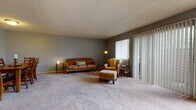 This single-floor residence offers a thoughtfully arranged layout with distinct living, dining, kitchen, and sleeping areas. The living room is generously sized, finished with plush wall-to-wall carpeting and cool grey walls that create a calm, neutral backdrop. Vertical blinds frame a sliding glass door that opens to an outdoor patio, allowing natural light to fill the space. A textured ceiling is consistent throughout the home, adding a classic touch.

The dining area sits adjacent to the living room, comfortably accommodating a full-sized dining table and chairs, with soft carpeting underfoot and simple, clean walls. The kitchen is equipped with warm honey-toned cabinetry, black appliances including a range, refrigerator, and dishwasher, complemented by a double basin sink and light tile flooring that is easy to maintain.

The bedroom is a comfortable, carpeted retreat featuring a natural window that brings in soft light, and a wide sliding-door closet with built-in shelving that provides ample storage. The full bathroom includes a tiled tub-shower combination, a vanity with storage, and neutral tile flooring, offering a clean and functional space. Overall, the home presents a practical and livable floor plan suited for everyday comfort.
