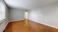 Located at 905 Montgomery Ave in the heart of Bryn Mawr, PA, this one-bedroom, one-bathroom residence offers a well-organized, efficient floor plan across a single level. The living room is a standout space, featuring warm parquet wood flooring in a classic herringbone-style pattern, neutral gray walls, and clean white trim that lend a timeless, polished character to the room. The bedroom continues the parquet flooring and offers dual windows that invite generous natural light, along with a wall-mounted air conditioning unit and radiator heating for year-round comfort. A dedicated closet provides practical storage. The galley-style kitchen is bright and functional, outfitted with white cabinetry, white countertops, and white appliances, including a range and refrigerator. Notably, the kitchen also accommodates a stacked in-unit washer and dryer — a convenient feature. Light wood-tone flooring completes the kitchen's clean aesthetic. The bathroom features classic white tile with a contrasting black accent border, and a full tub-shower combination. Two hallways connect the rooms, contributing to a logical and easy-to-navigate layout. Overall, the unit presents a clean, well-maintained interior with consistent finishes throughout.