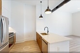 This contemporary 1-bedroom apartment in Bayonne, NJ offers 650 square feet of efficiently designed living space. The open-concept layout maximizes the use of space, seamlessly blending the living area with the kitchen. The sleek kitchen features wooden cabinetry, stainless steel appliances, and a spacious island with a sink, perfect for both meal preparation and casual dining.

The apartment boasts a minimalist aesthetic with crisp white walls and light wooden flooring throughout, creating a bright and airy atmosphere. Large windows in the living area and bedroom provide ample natural light and offer city views, enhancing the sense of spaciousness.

Industrial-inspired elements such as exposed ductwork and pendant lighting add character to the space. The bathroom, while not pictured, likely continues the modern design theme. A built-in closet in the bedroom offers practical storage solutions.

The property's location at 406 Bayonne, NJ 07002, combines urban convenience with a touch of suburban tranquility. This apartment is ideal for those seeking a contemporary living space with a thoughtful balance of style and functionality.