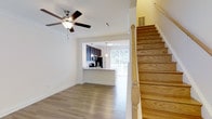 This three-story home offers a thoughtfully designed layout that balances comfort and functionality across multiple levels. The main living area greets you with an open-concept floor plan, showcasing smooth hardwood-style flooring, crisp white walls, and crown molding that adds a refined architectural touch. A ceiling fan with integrated lighting keeps the space comfortable and well-lit.

The kitchen flows seamlessly from the living area and is appointed with rich dark cabinetry, stainless steel appliances including a microwave and refrigerator, and a light-toned countertop peninsula that doubles as a breakfast bar. Pendant lighting hangs above the peninsula, providing both task lighting and a stylish focal point. A large window at the far end of the kitchen invites abundant natural light and offers views of the surrounding greenery, enhancing the overall brightness of the space.

A staircase with warm wood-toned treads and a classic newel post and railing connects the floors, providing an elegant transition between levels. The multi-story layout offers ample room for living, working, and entertaining, with each floor providing dedicated spaces to suit a variety of needs. The overall ambiance is clean, modern, and move-in ready.