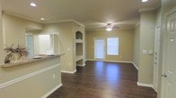 Located at 205 Benton Dr. in Allen, Texas, this single-story home offers a well-designed, open layout with thoughtful architectural details throughout. The living area is immediately welcoming, featuring rich dark hardwood floors that run throughout the main living space, complemented by crisp white crown molding and baseboards that frame the rooms with a clean, polished look. A ceiling fan with a light fixture anchors the center of the living room, providing both functionality and a classic finishing touch. Natural light filters in through windows dressed with white blinds, brightening the space with a warm, neutral ambiance reinforced by the soft beige wall tones. A standout architectural feature is the built-in display niche with an arched accent shelf, adding character and a convenient space for décor. The kitchen connects openly to the living area via a raised breakfast bar with a dark countertop, allowing for easy interaction between the two spaces. A pass-through window further enhances the open, connected feel of the home. The overall design balances practicality with comfort, offering a cohesive, move-in ready environment that suits a range of lifestyles in the heart of Allen, Texas.