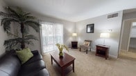 Located at 4101 Brett St, Unit E10 in Corpus Christi, Texas, this single-floor residence offers a functional and comfortable layout with thoughtfully designed living spaces throughout. The living room serves as the heart of the unit, featuring plush wall-to-wall carpeting and a large sliding glass door dressed with vertical blinds that floods the room with natural light and provides access to the outdoors. The open, airy atmosphere makes it an inviting space for both relaxing and entertaining. The kitchen is a standout feature, designed in a galley style with warm wood cabinetry lining both sides, dark granite-style countertops, and a full suite of appliances including a refrigerator, electric range, and dishwasher. A pass-through window connects the kitchen to the adjacent dining and living area, enhancing the open feel of the layout and making it ideal for everyday convenience. Hardwood-style flooring extends through the kitchen and hallway areas, adding a clean, polished contrast to the carpeted living spaces. A tall storage cabinet in the hallway provides ample organizational space. The bedroom is generously sized with soft carpeting, neutral walls, and a window that brings in natural light, creating a calm and restful retreat. Overall, the unit presents a clean, practical living environment in a residential Corpus Christi community.