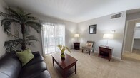 Located at 4101 Brett St, Unit E10 in Corpus Christi, Texas, this single-floor residence offers a functional and comfortable layout with thoughtfully designed living spaces throughout. The living room serves as the heart of the unit, featuring plush wall-to-wall carpeting and a large sliding glass door dressed with vertical blinds that floods the room with natural light and provides access to the outdoors. The open, airy atmosphere makes it an inviting space for both relaxing and entertaining. The kitchen is a standout feature, designed in a galley style with warm wood cabinetry lining both sides, dark granite-style countertops, and a full suite of appliances including a refrigerator, electric range, and dishwasher. A pass-through window connects the kitchen to the adjacent dining and living area, enhancing the open feel of the layout and making it ideal for everyday convenience. Hardwood-style flooring extends through the kitchen and hallway areas, adding a clean, polished contrast to the carpeted living spaces. A tall storage cabinet in the hallway provides ample organizational space. The bedroom is generously sized with soft carpeting, neutral walls, and a window that brings in natural light, creating a calm and restful retreat. Overall, the unit presents a clean, practical living environment in a residential Corpus Christi community.