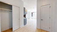 Located at 101 South Salina Street in the heart of downtown Syracuse, New York, this thoughtfully designed single-floor unit combines modern aesthetics with functional living. Light oak hardwood flooring runs throughout the space, creating a warm, cohesive foundation that complements the crisp white walls and clean architectural lines.

The kitchen is a standout feature, showcasing gray shaker-style cabinetry, a distinctive light blue subway tile backsplash, white quartz countertops, and a full suite of stainless steel appliances including a range, microwave, dishwasher, and refrigerator. Track lighting overhead adds both style and practicality to the cooking space.

The open living area is bathed in natural light, courtesy of large floor-to-ceiling windows that frame sweeping views of the Syracuse skyline and surrounding downtown architecture. The generous layout provides a versatile living space with ample room for a variety of configurations.

The bathroom is finished with neutral large-format tile flooring, a vanity with storage, and a glass-enclosed shower, accented by brushed gold grab bars that add an elegant touch. Additional interior doors provide access to closets and private areas, enhancing the overall functionality of the unit. The space offers a bright, contemporary urban living experience in a prime downtown location.