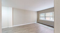 Located on North Prospect Avenue in Milwaukee's desirable East Side neighborhood, this one-bedroom, one-bathroom unit offers a well-planned layout across a single floor. The open kitchen and living area serves as the heart of the space, where light-toned luxury vinyl plank flooring runs throughout and neutral warm-beige walls create a clean, cohesive backdrop. The kitchen is outfitted with crisp white shaker-style cabinetry, granite-patterned countertops, a single-basin sink, and a full suite of stainless steel appliances including a refrigerator, dishwasher, and range with overhead microwave. The living room receives natural light through a wide multi-pane window framed by baseboard heating, giving the room a bright and comfortable feel. A hallway with an intercom panel connects the main living area to the private spaces. The bedroom features plush carpeting, a ceiling light fixture, a window with blinds, and baseboard heating for year-round comfort. The bathroom retains charming vintage character with soft green ceramic wall tiles, warm terra cotta mosaic tile flooring, a white vanity with mirror, and a classic toilet, all accented by bright overhead lighting. The unit offers a compact yet functional living experience in a well-connected Milwaukee location.