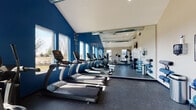 Located at 2800 John Steven Way in Reynoldsburg, Ohio, this single-floor fitness facility is designed to support an active lifestyle with a thoughtfully arranged layout and quality amenities throughout.

The centerpiece of the space is a bright, open fitness room with striking bold blue accent walls and vaulted ceilings that create an energizing atmosphere. A row of TRUE-brand treadmills lines the floor alongside upright and recumbent cardio bikes, while strength training equipment and cable machines are visible toward the rear. Floor-to-ceiling mirrors along one wall visually expand the space and allow users to monitor their form. Large windows along the side wall flood the gym with natural light and offer views of the surrounding outdoor landscape. Exposed ductwork and a ceiling fan add an industrial yet functional touch to the overall aesthetic.

The restroom is finished with considerable detail, featuring a decorative mosaic tile accent wall in a blend of earthy gray and taupe tones that adds visual texture and depth. A pedestal sink with brushed nickel fixtures sits beneath a framed mirror, and the muted gray walls create a calm, neutral backdrop. Dark wood-paneled doors with classic raised panels complete the interior, contributing a grounded, cohesive feel to the space. Together, these areas combine practicality with polished design.