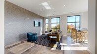 Located at 1835 Morehead Ridge Dr in Charlotte, NC, this single-floor community lounge space delivers a polished, contemporary design with a thoughtful mix of textures and finishes. The main gathering area centers around a comfortable seating arrangement — featuring a tan sofa, teal accent chairs, and a patterned area rug — all anchored beneath recessed lighting and set against a striking full-height textured tile accent wall with a wall-mounted flat-screen television. Light wood-look flooring and large-format tile create a dynamic, layered foundation throughout the space. Oversized black-framed windows flood the interior with abundant natural light while framing vivid views of autumn foliage and the Charlotte skyline beyond. A dedicated wet bar area, complete with dark countertops and teal cabinetry, provides a convenient hospitality station. A high-top dining table with wooden bar stools is positioned at the window-lined corner, offering an elevated vantage point of the surrounding landscape. Expansive glass French doors lead directly to a furnished outdoor terrace, seamlessly extending the entertaining space and providing sweeping open-air views of the Charlotte cityscape — making this lounge an exceptional venue for both relaxation and social gatherings.