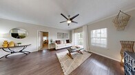Located at 11400 Gables Dr in Fishers, Indiana, this 2-bedroom, 2-bathroom residence offers a thoughtfully designed single-floor layout that balances comfort and functionality. The living room serves as the heart of the home, featuring rich dark hardwood-style flooring, crown molding, a modern ceiling fan, and large sliding glass doors that flood the space with natural light and provide access to an outdoor area. Adjacent to the living room, the dining area is defined by a pendant light fixture and crown molding, with an open pass-through connecting seamlessly to the kitchen. The kitchen is equipped with white shaker-style cabinetry, granite-look countertops, and black appliances including a range, over-the-range microwave, and refrigerator. Both bedrooms are carpeted and feature ceiling fans and closets, with the primary bedroom offering a generously sized layout and natural light from a well-positioned window. The bathrooms are finished with white cabinetry, granite-look countertops, and hardwood-style flooring, providing a clean and modern aesthetic. Two closets offer ample storage throughout the residence. The neutral color palette and consistent finishes create a cohesive, inviting ambiance suited for everyday living.