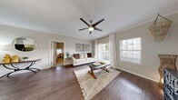 Located at 11400 Gables Dr in Fishers, Indiana, this 2-bedroom, 2-bathroom residence offers a thoughtfully designed single-floor layout that balances comfort and functionality. The living room serves as the heart of the home, featuring rich dark hardwood-style flooring, crown molding, a modern ceiling fan, and large sliding glass doors that flood the space with natural light and provide access to an outdoor area. Adjacent to the living room, the dining area is defined by a pendant light fixture and crown molding, with an open pass-through connecting seamlessly to the kitchen. The kitchen is equipped with white shaker-style cabinetry, granite-look countertops, and black appliances including a range, over-the-range microwave, and refrigerator. Both bedrooms are carpeted and feature ceiling fans and closets, with the primary bedroom offering a generously sized layout and natural light from a well-positioned window. The bathrooms are finished with white cabinetry, granite-look countertops, and hardwood-style flooring, providing a clean and modern aesthetic. Two closets offer ample storage throughout the residence. The neutral color palette and consistent finishes create a cohesive, inviting ambiance suited for everyday living.