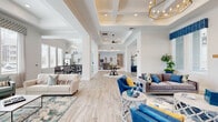 This single-floor community amenity space is thoughtfully designed to offer residents a refined and functional gathering environment. The grand entryway welcomes visitors with striking large-format marble-look tile flooring, soaring ceilings with crown molding, and glass entry doors that flood the foyer with natural light.

The centerpiece of the facility is a spacious open-concept lounge area featuring light hardwood-style flooring, coffered ceilings with recessed lighting, and an elegant gold chandelier. The seating area is furnished with a mix of plush sofas and vibrant blue accent chairs, creating a welcoming and sophisticated atmosphere.

Adjacent to the lounge is a well-equipped kitchen outfitted with gray shaker cabinetry, a patterned tile backsplash, marble countertops, and stainless steel appliances. A separate dining area features large windows with abundant natural light, marble tile flooring, and a communal dining table with contemporary upholstered seating.

The expansive fitness center is divided into multiple zones, including a cardio area lined with treadmills and ellipticals, a strength training section with cable machines and free weights, and a dedicated functional training room with exercise balls and specialty equipment. Tray ceilings, ceiling fans, and large windows throughout the fitness spaces create a bright and airy workout environment. Restroom facilities are also conveniently located within the space.