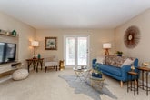 This single-floor residence offers a thoughtfully arranged layout across several distinct living areas. The living room serves as the central gathering space, featuring carpet flooring, a textured ceiling, and a sliding glass door and French doors that invite natural light and provide access to an outdoor area. A built-in media shelf adds a functional architectural detail to the room.

Adjacent to the living room, a dedicated dining area accommodates a four-seat table beneath a ceiling fan, with wood-style flooring that continues into the galley-style kitchen. The kitchen is efficiently designed with cabinetry on both sides, stainless steel appliances, and a double sink with ample counter space.

The primary bedroom is generously sized with carpet flooring, vaulted ceilings, and windows that allow natural light. It connects to a private bathroom featuring wood-style flooring, a single vanity, and storage cabinetry. A second bedroom, also carpeted and well-lit by large windows, includes a closet and access to a second full bathroom, also finished with wood-style flooring and a vanity. The overall palette throughout is neutral and warm, creating a cohesive and inviting atmosphere.