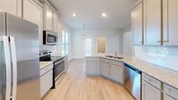 Located at 990 Perth Rd in Mooresville, NC, this two-story home offers a thoughtfully designed layout with quality finishes throughout. The main level features light hardwood-style flooring that flows through the open living areas. The kitchen is a standout space, equipped with gray shaker-style cabinetry, granite countertops, stainless steel appliances, a tile backsplash, and a central island with a built-in sink — ideal for both cooking and entertaining. A powder room on the main level includes a classic pedestal sink with an oval mirror. Decorative wainscoting with board-and-batten paneling adds architectural character to the dining or flex area, complemented by large windows that invite natural light. A striking staircase with wood handrails and wrought iron balusters connects the two floors, rising through a soaring two-story space filled with natural light from stacked windows. Upstairs, the primary bedroom features a tray ceiling with crown molding and a ceiling fan, plush carpeting, and multiple windows. Additional bedrooms are carpeted and include walk-in closets and windows overlooking the surrounding neighborhood. The home presents a clean, neutral palette throughout, making it a versatile and move-in-ready residence.