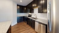 This single-floor unit at 408 Eddie Dowling Highway in North Smithfield, Rhode Island, offers a well-designed layout with modern finishes throughout. The kitchen is a standout feature, equipped with dark espresso cabinetry extending to the ceiling, granite countertops, a subway tile backsplash, and stainless steel appliances including a range, microwave, and dishwasher. The hardwood flooring in the kitchen flows into the open living area, which is bright and airy, featuring a large glass door that opens to a private balcony overlooking lush greenery—bringing in generous natural light. The bedroom is comfortably sized, featuring plush wall-to-wall carpeting and two windows that provide additional outdoor views and natural light. The bathroom is finished with a classic black-and-white hexagonal mosaic tile floor, a dark-vanity with a white countertop, an oversized mirror, and clean white walls that contribute to a crisp, timeless aesthetic. A dedicated laundry area houses a stacked GE front-load washer and dryer unit, adding convenience to everyday living. Throughout the space, neutral wall tones and consistent trim details create a cohesive and polished ambiance.