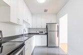 Located at 10 Garfella Dr in Toronto's M9V neighbourhood, this two-bedroom, one-bathroom unit offers a practical and well-maintained single-floor layout. Throughout the living areas and bedrooms, warm-toned parquet flooring adds a classic character that contrasts cleanly with the crisp white walls and trim.

The spacious primary bedroom is a standout feature, offering generous proportions and large windows that frame views of mature trees and the surrounding greenery, filling the room with natural light. A baseboard heating unit runs beneath the windows, ensuring year-round comfort. The second bedroom is equally bright, with the same consistent parquet flooring and clean, neutral finishes.

The kitchen is functional and modern, featuring white cabinetry, dark countertops, and a stainless steel refrigerator. Tile flooring in the kitchen provides a practical transition from the parquet of the living areas. The layout flows efficiently, with a central hallway connecting the main living space, bedrooms, and kitchen.

The bathroom is finished with classic white subway tile surrounding a full soaker tub and shower combination, accented by chrome fixtures for a timeless, clean aesthetic. Overall, the unit presents a bright, tidy, and move-in ready space ideal for those seeking comfortable urban living in Toronto's west end.