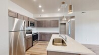 Located on W Deadwood Ave in Rathdrum, Idaho, this well-appointed 3-bedroom, 2-bathroom residence offers a thoughtfully designed single-floor layout. The open-concept kitchen serves as the heart of the home, featuring rich dark wood cabinetry, quartz countertops, stainless steel appliances including a refrigerator, range, and microwave, and a central island with a sink and stylish pendant lighting overhead. Light wood-style plank flooring runs throughout the main living areas, contributing to a clean, contemporary aesthetic. The spacious living room is filled with natural light from large windows that frame views of the surrounding neighborhood and distant mountains, with a sliding glass door providing outdoor access. The three bedrooms are finished with plush carpeting, and the generously sized primary bedroom features dual closets with built-in wire shelving, offering ample storage. Both bathrooms are finished consistently with the rest of the home, showcasing dark wood vanities, quartz countertops, large mirrors with modern lighting fixtures, and light wood-style flooring. A hallway connects the living spaces to the private bedrooms and bathrooms, providing a functional and organized flow throughout the residence.