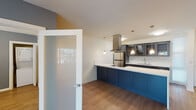 This well-appointed single-floor unit offers a thoughtfully designed layout that balances style and function. The open kitchen is a standout feature, showcasing bold navy blue cabinetry paired with a striking white quartz countertop and coordinating marble-look backsplash. A large central island provides generous prep and dining space, while a sleek stainless steel range hood serves as a focal point above stainless steel appliances, including a refrigerator and dishwasher. Dark upper cabinets with glass-front doors add depth and display storage. The living area features warm wood-look flooring, cool blue-grey accent walls, and a ceiling fan, with sliding glass doors that invite natural light and outdoor access. A second bedroom or flex space echoes the same palette and includes a ceiling fan and a convenient in-unit stacked washer and dryer closet. The bathrooms are tastefully finished: one features warm travertine-style tile surrounding a soaking tub with sliding glass doors, while the other offers a sleek dark vanity with white quartz countertop and a tiled walk-in shower. Throughout the unit, consistent wood-look flooring, neutral white walls, and modern finishes create a cohesive and contemporary living environment.