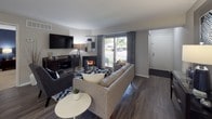 The Wedgewood Deluxe is a thoughtfully designed 2-bedroom, 2-bathroom single-floor residence that balances comfort and modern style. The living room serves as the heart of the home, featuring rich hardwood-style flooring, a cozy fireplace, and a sliding glass door that fills the space with natural light and provides views of the surrounding greenery. The open layout flows seamlessly into a dining area and a well-appointed kitchen, which boasts white cabinetry, a gray tile backsplash, sleek quartz countertops, stainless steel appliances, and a deep undermount sink. Both bedrooms are generously sized and finished with plush carpeting. The primary bedroom features a walk-in closet and direct access to an en-suite bath. The second bedroom offers bright natural light through large windows. Each bathroom is finished with wood-look vinyl flooring, quartz vanity countertops, white cabinetry, and a tub-shower combination. A convenient in-unit stacked washer and dryer adds everyday practicality. Throughout the residence, neutral tones and clean lines create a calm, cohesive ambiance suited for comfortable living.