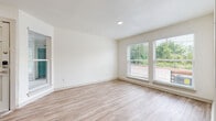 This single-floor unit features a clean, modern design highlighted by light hardwood-style flooring that flows consistently throughout. The open living area is generously sized, bathed in natural light from multiple windows fitted with blinds that frame views of surrounding greenery. A stylish steel-framed glass door adds an industrial accent, connecting the main living space to an adjacent area.

The kitchen is outfitted with white shaker-style cabinetry, light quartz countertops, a stainless steel sink, and a full suite of stainless steel appliances including a refrigerator, electric range, over-the-range microwave, and built-in oven. The layout offers ample counter and cabinet space for everyday use.

The bedrooms each include hardwood-style flooring, ceiling fans, and windows providing natural light and outdoor views. One bedroom features a sliding closet, while another benefits from a quiet corner layout.

The bathroom is finished with warm beige subway tile surrounding a full soaking tub and shower combination, complemented by brushed nickel fixtures and hardwood-style flooring. The overall ambiance across the unit is fresh, neutral, and move-in ready.