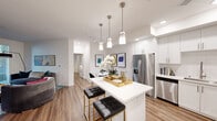 This thoughtfully designed 2-bedroom, 2-bathroom residence offers a bright and modern living experience across a single floor. The open-concept layout seamlessly connects the kitchen, dining, and living areas, creating a cohesive and functional space. The kitchen is a standout feature, showcasing white shaker cabinetry extending to the ceiling, quartz countertops, a full suite of stainless steel appliances including a gas range, microwave, dishwasher, and French door refrigerator, and a central island with pendant lighting overhead — ideal for casual dining or entertaining. The adjacent dining area provides an intimate setting with clean white walls. The living room offers a bold teal accent wall, wood-look flooring, and large glass doors that invite natural light and outdoor views. Both bedrooms are comfortably sized, with the primary bedroom featuring wood-look floors and ample natural light from well-positioned windows. Each bathroom is finished with white vanity cabinetry, quartz countertops, undermount sinks, and large mirrors. Consistent wood-look flooring flows throughout the entire residence, tying together a clean, contemporary aesthetic. A closet and hallway complete the well-organized floor plan.