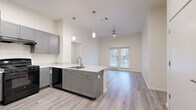 This 3-bedroom, 2-bathroom single-story residence in Austin, TX offers a thoughtfully designed open-concept layout. The kitchen serves as the centerpiece of the main living area, featuring gray shaker-style cabinetry, light stone countertops, a peninsula with an integrated sink, pendant lighting, and black appliances including a refrigerator and range. The kitchen flows seamlessly into the living area, which is brightened by natural light from French doors and accented by a ceiling fan overhead. Light-toned wood-look flooring runs throughout the main living spaces, adding warmth and continuity. The three bedrooms are carpeted and offer neutral white walls, providing a clean, versatile canvas. The primary bedroom includes a walk-in closet with built-in shelving and hanging rods. Both bathrooms are well-appointed with gray vanities, marble-style countertops, wood-look vinyl flooring, and tub-shower combinations featuring warm earth-toned tile surrounds and curved shower rods. Additional storage closets are visible near the entryway. The overall aesthetic is modern and understated, with a neutral color palette throughout that creates a bright, cohesive living environment suited for a variety of lifestyles.