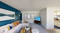 This thoughtfully laid-out 2-bedroom, 1-bathroom single-floor residence makes excellent use of its space across a cohesive and stylish floor plan. The living room serves as the heart of the home, anchored by a striking deep teal accent wall that adds a bold pop of color against light gray walls and soft carpeted flooring. A sectional sofa, warm brass wall sconce, and curated artwork create an inviting and contemporary atmosphere with natural light filtering in through a large window near the entryway. Adjacent to the living room, the dining area features a live-edge wood dining table, ceiling fan, and large windows that frame outdoor greenery, filling the space with ample daylight. The galley-style kitchen is equipped with white cabinetry trimmed in warm wood tones, granite-look countertops, and wood-look flooring, offering functional efficiency in a compact layout. In-unit laundry is also accommodated within the kitchen area. The primary bedroom is a serene retreat, continuing the teal accent wall theme, with multiple windows, plush carpet, and a double-door closet providing generous storage. The second bedroom mirrors this comfortable aesthetic. The shared bathroom features a tub-shower combo with sliding glass doors, a white vanity, and wood-look tile flooring, offering a clean and practical finish throughout.