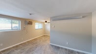 This single-floor unit offers a practical and well-organized layout finished with consistent large-format tile flooring throughout every room, lending a cohesive and easy-to-maintain aesthetic. The neutral beige and gray tones on the walls complement the flooring, creating a clean, understated palette across the space.

The main living area is generously sized, featuring a ceiling fan, a wall-mounted air conditioning unit, and multiple windows that allow natural light to fill the room. A secondary open area adjacent to the living space provides additional flexibility for various uses.

The kitchen is equipped with warm-toned oak cabinetry offering ample upper and lower storage, a dark countertop, a double-basin sink, a white electric range, and a full-size refrigerator, all illuminated by overhead lighting.

The bedroom includes a built-in closet and connects to an adjacent room, providing added versatility. Wall-mounted heating and cooling units are present in multiple rooms, ensuring climate control throughout. The bathroom is clean and simply appointed, featuring a white vanity with an integrated sink, a wall mirror, and a towel bar. The space is completed by a private entry door, offering direct access to the unit.