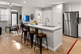 This two-bedroom, two-bathroom unit at 3145 Market St in Riverside, California offers a well-designed, single-story layout with modern finishes throughout. The open-concept kitchen is a central highlight, featuring white shaker-style cabinetry with ample storage, quartz countertops, a stainless steel refrigerator, gas range, and microwave. A spacious kitchen island with a built-in sink doubles as a breakfast bar with seating, seamlessly connecting the kitchen to the living and dining areas. Light wood-style flooring runs throughout the common areas, lending a clean, contemporary feel. The living room is bright and welcoming, benefiting from large windows with blinds, a ceiling fan, and direct access to a private patio. Both bedrooms are comfortably sized with natural light from windows and easy access to closet space. The primary bathroom includes a dual-sink vanity with quartz countertops and a shower/tub combo, while the second bathroom offers a similarly clean design with a walk-in closet adjacent. Recessed lighting throughout the unit adds to the modern aesthetic, and the neutral color palette creates a cohesive, move-in-ready atmosphere.