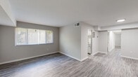 This single-floor unit offers a clean, modern aesthetic throughout, unified by durable wood-look vinyl plank flooring and a neutral gray-and-white color palette. The open living area is generously proportioned, filled with natural light from a large window fitted with horizontal blinds, and connects seamlessly to the rest of the unit. A wall-mounted HVAC vent provides climate control, and clean white baseboards frame each room with a crisp finish.

The kitchen is efficiently designed with white shaker-style cabinetry, granite-pattern countertops, a stainless steel sink, and black appliances including a gas range and refrigerator. A window above the cooking area allows natural light to brighten the workspace.

The bedroom is a comfortable, well-sized retreat featuring a window overlooking greenery, a ceiling light fixture, and notably, two closets — one a full-depth wardrobe with built-in shelving and hanging rod, offering excellent storage capacity. An additional spacious room with recessed lighting provides flexible use as a second bedroom, office, or den.

The bathroom is finished in crisp white, featuring a single-sink vanity with brushed nickel fixtures, a framed mirror, and a tiled shower-tub combination. The overall space is clean, functional, and move-in ready.