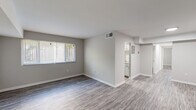 This single-floor unit offers a clean, modern aesthetic throughout, unified by durable wood-look vinyl plank flooring and a neutral gray-and-white color palette. The open living area is generously proportioned, filled with natural light from a large window fitted with horizontal blinds, and connects seamlessly to the rest of the unit. A wall-mounted HVAC vent provides climate control, and clean white baseboards frame each room with a crisp finish.

The kitchen is efficiently designed with white shaker-style cabinetry, granite-pattern countertops, a stainless steel sink, and black appliances including a gas range and refrigerator. A window above the cooking area allows natural light to brighten the workspace.

The bedroom is a comfortable, well-sized retreat featuring a window overlooking greenery, a ceiling light fixture, and notably, two closets — one a full-depth wardrobe with built-in shelving and hanging rod, offering excellent storage capacity. An additional spacious room with recessed lighting provides flexible use as a second bedroom, office, or den.

The bathroom is finished in crisp white, featuring a single-sink vanity with brushed nickel fixtures, a framed mirror, and a tiled shower-tub combination. The overall space is clean, functional, and move-in ready.
