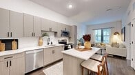 Located at 1720 Nick Nuccio Parkway in Tampa, FL, this thoughtfully designed one-bedroom, one-bathroom residence offers a modern living experience with efficient use of space across a single floor. The open-concept kitchen and living area serves as the heart of the home, featuring a sleek kitchen outfitted with gray flat-front cabinetry, white quartz countertops, a herringbone tile backsplash, and a full suite of stainless steel appliances. A central island with bar seating provides additional prep space and casual dining. Wood-look flooring flows throughout, adding warmth and continuity. The living room receives natural light through large windows and offers a comfortable, well-proportioned layout. The bedroom is a serene retreat, featuring generous windows with views to the outdoors, and direct access to a dedicated closet. The full bathroom presents a clean, contemporary aesthetic with light wood cabinetry, white countertops, dark hardware accents, and a tub-shower combination with crisp white tile surround. Throughout the residence, white walls and recessed lighting create a bright, airy ambiance that complements the modern design sensibility.