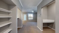 This single-story, 4-bedroom, 1-bathroom home offers a functional and comfortable layout designed to maximize everyday living. The combined kitchen and living room serves as the heart of the home, where the kitchen features white cabinetry, light stone countertops, a tile backsplash, and a full suite of stainless steel appliances including a range, microwave, and refrigerator, all set on easy-care wood-look flooring. The living area extends naturally from the kitchen, adorned with crown molding, a ceiling fan, and large windows and a glass door that allow abundant natural light and views of lush greenery outside. The bedrooms are carpeted in warm neutral tones, each featuring large windows with outdoor views, providing a bright and airy atmosphere. The generously sized primary bedroom includes access to a spacious walk-in closet outfitted with wire shelving along multiple walls for ample storage. The bathroom is cleanly finished with a white vanity, stone countertop, and a full tub-shower combo with tile surround and wood-look flooring. A dedicated laundry area accommodates a full-size washer and dryer. Two hallways connect the rooms efficiently, completing this practical and well-designed home.