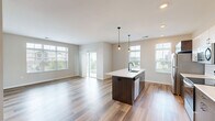 This well-appointed 2-bedroom, 2-bathroom single-floor residence showcases a clean, contemporary design throughout. The heart of the home is an open-concept kitchen and living area bathed in natural light from multiple large windows. The kitchen is equipped with stainless steel appliances, a subway tile backsplash, two-tone cabinetry featuring white upper cabinets and gray lower cabinets, and a dark-finished island with a built-in sink and pendant lighting above. Durable wood-look flooring flows seamlessly through the main living areas, adding warmth to the modern aesthetic. The living area extends to a private balcony through a sliding glass door, offering outdoor views and additional natural light. Both bedrooms feature plush carpeting and ample natural light from well-sized windows. The primary bedroom includes a walk-in closet with wire shelving. The primary bathroom offers a sleek vanity with dark wood cabinetry and a glass-enclosed walk-in shower, while the second bathroom features a full soaking tub and shower combination with matching cabinetry. A hallway and dedicated closet provide additional storage. Recessed lighting and black hardware accents complete the modern, cohesive look of this thoughtfully designed residence.