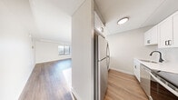 Located at 68 Pearl St in Brookline, MA, this one-bedroom, one-bathroom residence offers a well-designed single-floor layout with a clean, modern aesthetic throughout. Warm hardwood-style flooring flows seamlessly across all living areas, complementing the crisp white walls and neutral tones that give the space a bright, airy feel.

The open living area is generously proportioned and receives natural light through a large window, creating a welcoming atmosphere. It connects intuitively to the kitchen via a pass-through counter, enhancing the open-plan feel. The galley-style kitchen is efficiently organized and outfitted with stainless steel appliances — including a full-size refrigerator, range, and microwave — paired with white shaker cabinetry, a white countertop, and a matte black faucet.

The bedroom is a well-sized private retreat featuring a window with views of the surrounding Brookline neighborhood. It includes an organized closet system with shelving, offering practical storage. A hallway connects the main living spaces to the full bathroom, which features a white soaking tub and shower combination with matte black fixtures, maintaining the consistent modern design language found throughout the residence.