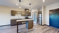This single-floor unit presents a contemporary design with a neutral color palette and thoughtful finishes throughout. The kitchen serves as a central highlight, showcasing dark wood-toned cabinetry, granite countertops, and a full suite of stainless steel appliances, including a range, microwave, dishwasher, and refrigerator. A central island with bar-height seating provides additional prep space and casual dining. Pendant lighting and recessed ceiling fixtures illuminate the kitchen, while a frosted-glass door adds a stylish architectural detail nearby. Wood-look plank flooring extends through the kitchen and into the adjacent dining area, which features a classic chandelier overhead.

The bedrooms are finished with plush carpeting and include ceiling fans for comfort. Closet storage is present, with wire shelving visible in at least one bedroom. The bathroom is clean and functional, featuring a full soaking tub with shower, granite-topped vanity with dark cabinetry, and wood-look tile flooring consistent with the unit's overall aesthetic. Additional carpeted rooms offer flexible use options. Throughout, the space maintains a cohesive, modern character with consistent trim work and a bright, neutral finish.