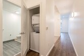 Located at 19550 Vallco Parkway in Cupertino, CA, this thoughtfully designed single-floor unit offers a clean, contemporary aesthetic throughout. The open kitchen is a standout feature, showcasing a two-tone cabinet layout with crisp white uppers and rich dark-brown lower cabinets, stainless steel appliances including a gas range, dishwasher, and built-in microwave, complemented by a sleek under-cabinet range hood and a single-basin sink. Light hardwood-style flooring runs throughout the main living areas, enhancing the bright, modern feel. The hallways are well-proportioned and include a dedicated in-unit laundry closet with a stacked washer and dryer — a practical convenience. The bedroom features plush neutral carpeting, a sliding-door closet with built-in rod, and a large window that frames views of the surrounding Cupertino neighborhood, allowing generous natural light to fill the room. The bathroom is finished with large-format light gray tile flooring, a floating dark-wood vanity with an integrated white sink, a framed mirror, and clean white walls that create a crisp, spa-like atmosphere. Overall, the space presents a well-organized, efficiently utilized layout with modern finishes suited to comfortable urban living in the heart of Silicon Valley.