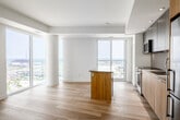 Located at 131 Mill St in Toronto's vibrant Leslieville neighbourhood, this modern 2-bedroom, 2-bathroom unit offers a thoughtfully designed open-concept layout with clean, contemporary finishes throughout. Light hardwood flooring flows seamlessly across all living areas, complementing the bright, neutral colour palette.

The combined kitchen and living room serves as the heart of the unit. The kitchen features two-tone cabinetry — matte grey uppers paired with warm wood-grain lowers — along with a sleek quartz island, stainless steel appliances, and a glass tile backsplash. A linear pendant light adds a refined touch. Floor-to-ceiling windows bathe the living area in natural light and frame expansive panoramic views of the Toronto skyline and surrounding greenery.

Both bedrooms continue the light hardwood flooring and bright aesthetic, with large windows offering generous natural light and impressive elevated views. Recessed lighting provides a polished finish in each room.

The two bathrooms are well-appointed: one features a glass-enclosed walk-in shower with grey tile surround and warm wood cabinetry, while the second includes a soaker tub with large-format marble-look tile. A clean, bright hallway with recessed lighting connects all rooms efficiently, completing this well-appointed urban residence.