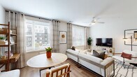 This efficient yet thoughtfully designed 1-bedroom, 1-bathroom residence offers a functional single-floor layout encompassing a living room, kitchen, bedroom, bathroom, hallway, and closet. The open-concept living and dining area is bathed in natural light from multiple large windows dressed with patterned curtains and horizontal blinds, offering views of the surrounding neighborhood. Light wood-tone flooring flows throughout the main living spaces, while a ceiling fan adds comfort overhead. The galley-style kitchen is a standout feature, showcasing charcoal-gray cabinetry extending to the ceiling, sleek white quartz countertops, a subway tile backsplash, stainless steel appliances including a French door refrigerator and range, and recessed lighting. The bedroom provides a comfortable retreat with carpeted flooring, a dedicated closet with built-in shelving and hanging rods, and direct access to the hallway. The full bathroom is finished with light tile flooring, a dark-toned vanity with a white countertop, a tub-shower combination with white tile surround, and recessed lighting, creating a clean and contemporary feel throughout.