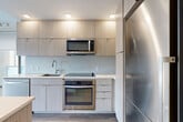 Located at 301 M St SW, Unit 503 in Washington, DC, this two-bedroom, one-bathroom residence offers a well-designed layout with a clean, contemporary aesthetic. The modern kitchen is a standout feature, outfitted with light wood-grain cabinetry extending to the ceiling, stainless steel appliances including a refrigerator, electric range, built-in microwave, and dishwasher, along with light quartz countertops and a subtle tile backsplash. Wood-look flooring runs throughout the unit, lending warmth and continuity across spaces. The living and dining areas are positioned to maximize the flow of the home, with a glass partition wall adding an architectural element that allows natural light to pass between rooms. Both bedrooms are well-proportioned, each featuring large windows with roller shades that frame views of the surrounding greenery. Exposed concrete columns add an industrial character that contrasts nicely with the otherwise soft, neutral palette. The bathroom is finished with large-format light tile flooring, a wall-mounted vanity with mirror, and a glass-enclosed walk-in shower. Additional highlights include in-unit laundry, three closets for ample storage, and a private balcony — a rare outdoor amenity in the heart of the city.