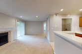 This single-floor space is designed with an open, functional layout that connects the main living areas seamlessly. The living room serves as the centerpiece, finished with plush wall-to-wall carpeting, crown molding, and recessed lighting that evenly illuminates the space. A tile-surround fireplace with a white mantel anchors one wall, while a large sliding glass door fitted with vertical blinds allows natural light to pour in and provides outdoor access. An additional window further brightens the room.

The kitchen is accessible via a pass-through counter that opens toward the living area, offering a practical connection between the two spaces. Warm wood cabinetry, light countertops, tile flooring, and a full suite of stainless steel appliances—including a gas range, refrigerator, and dishwasher—equip the kitchen for everyday use.

The bedroom features neutral carpeting, a window with blinds for natural light and privacy, and a ceiling light fixture. The bathroom includes a wood-toned vanity with a stone-finish countertop and integrated sink, a large wall mirror, and a combined tub and shower. Throughout the unit, neutral gray walls, white trim, and consistent finishes create a clean, cohesive aesthetic.