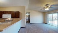 This single-floor residence offers a thoughtfully designed layout that balances comfort and functionality. The open-concept living area is generously proportioned, featuring plush wall-to-wall carpeting, a ceiling fan with light fixture, and a vaulted ceiling section that adds an airy sense of volume. A sliding glass door leads to a private balcony, flooding the space with natural light and providing pleasant outdoor views.

The kitchen is well-equipped and efficient, showcasing rich dark-stained cabinetry with brushed nickel hardware, light laminate countertops, a double stainless steel sink, and white appliances including a range and over-the-range microwave. Durable tile-style flooring runs throughout the kitchen, which connects seamlessly to the living area via a raised breakfast bar.

The bedrooms are carpeted and comfortably sized, each featuring ceiling fans and wall-mounted air conditioning units. One bedroom includes a walk-in closet, while windows provide natural light and neighborhood views. Baseboard heating is present throughout the unit for year-round comfort.

Two full bathrooms serve the residence. One features a walk-in shower, dark vanity cabinetry, and tile flooring, while the second offers a full tub-shower combination, a matching dark vanity, and the same durable tile flooring. Both bathrooms are clean and functional in design.