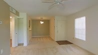 This single-floor residence offers a straightforward and functional layout designed for comfortable everyday living. The open-plan living and dining area forms the heart of the home, creating a seamless flow between spaces. The living area features plush wall-to-wall carpeting underfoot and is equipped with a ceiling fan, providing both comfort and air circulation. Natural light filters in through a window fitted with blinds, brightening the interior with a soft, neutral ambiance. The walls are painted in a warm, muted tone that complements the light-colored carpeting and white trim throughout. A dedicated entryway with a solid white door and a dark tile threshold provides a clear transition from outside to inside. Adjacent to the living area, the dining space is distinguished by a stylish pendant light fixture that hangs overhead, adding a touch of warmth and definition to the area. A pass-through or open connection to the kitchen is visible, enhancing the open feel of the layout. The textured ceiling adds subtle visual interest and is consistent throughout the space. Overall, this residence presents a clean, neutral, and move-in ready environment with a cohesive design that is both practical and welcoming.