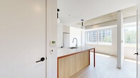Located at 1201 Rue de la Montagne in the heart of downtown Montréal, this thoughtfully designed unit offers a clean, contemporary aesthetic across a single floor. Light hardwood flooring runs throughout, complementing the crisp white walls and lending warmth to the space.

The open-concept kitchen is a standout feature, anchored by a central island with a white quartz countertop, warm wood cabinetry, and terracotta-toned metal accents. Pendant globe lights hang above the island, adding a modern touch. The kitchen is equipped with stainless steel appliances, including a refrigerator, stove, and built-in microwave, alongside a subway tile backsplash and ample upper cabinetry. A stacked washer and dryer unit is conveniently integrated nearby.

The living area benefits from a large window that frames views of the surrounding urban landscape, allowing natural light to flood the space. Exposed concrete ceiling details add an industrial character that contrasts elegantly with the otherwise minimalist interior.

The bathroom is finished to a high standard, featuring large-format white wall tiles, a frameless glass-enclosed shower, a floating vanity with an undermount sink, and globe pendant lighting that echoes the kitchen's design language. The overall ambiance is bright, clean, and functional — ideal for urban living in one of Montréal's most vibrant neighborhoods.