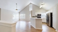 This thoughtfully designed 1-bedroom, 1-bathroom single-floor residence offers an efficient and comfortable layout. The open-concept living and kitchen area is the centerpiece of the home, distinguished by dramatic vaulted ceilings that create a striking sense of vertical space and airiness. A ceiling fan with a brushed gold finish anchors the living area, which features warm hardwood-style flooring and multiple windows dressed with blinds, allowing abundant natural light to pour in. A charming round accent window adds architectural character to the space.

The kitchen is well-equipped with a full suite of stainless steel appliances, including a refrigerator, range, and over-the-range microwave. White shaker-style cabinetry, grey subway tile backsplash, and light countertops complement the clean, modern aesthetic. A peninsula island provides additional prep and seating space.

The bedroom is a comfortable retreat, finished with plush carpeting, a ceiling fan, and a window offering views of the outdoors. The full bathroom features wood-look flooring, a tiled tub-shower combination, a white vanity with ample counter space, and brushed nickel hardware throughout. A hallway connects the private areas of the home, completing this well-organized and inviting layout.