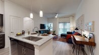 Located on E Wonsley Drive in Austin, TX, this single-story residence offers a thoughtfully designed open-concept floor plan with contemporary finishes throughout. The kitchen serves as a central hub, featuring dark espresso cabinetry, granite countertops, stainless steel appliances including a French door refrigerator, microwave, and range, as well as a large island with bar seating and elegant pendant lighting overhead. Light wood-style flooring flows seamlessly from the kitchen into the spacious living area, where a ceiling fan, large sliding glass door, and vertical blinds allow abundant natural light and outdoor access. The living room provides a welcoming atmosphere accentuated by decorative wall panels and a cozy sectional seating arrangement. The bedrooms are comfortably scaled, each with windows dressed in layered blinds and curtains, offering a restful ambiance. The bathrooms are finished with granite-topped dark vanities, tub-shower combinations with white tile surrounds, and wood-style flooring. Crown molding and arched doorways lend architectural character throughout. The overall aesthetic is modern and cohesive, combining neutral tones with warm accents for a comfortable, livable environment.