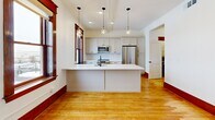Located at 1701 Milton Ave in Solvay, NY, this single-floor 2-bedroom, 1-bathroom residence blends classic architectural character with modern updates. Warm hardwood floors and rich dark wood trim run throughout, creating a cohesive and inviting aesthetic. A central hallway connects the living spaces, flanked by two closets for ample storage.

The kitchen is a standout feature, offering a large central island with a white quartz countertop, undermount sink, and pendant lighting. Shaker-style cabinetry, a subway tile backsplash, and stainless steel appliances — including a refrigerator, range, and microwave — complete the space. Multiple windows with deep-toned wood trim flood the kitchen with natural light and provide views of the surrounding neighborhood.

Both bedrooms are generously sized, each featuring hardwood floors, bright windows with classic trim, and a clean, neutral palette. The spacious primary bedroom offers particularly comfortable proportions. The bathroom is thoughtfully designed with a black-and-white tile floor, a tiled walk-in shower with black accent trim, and brushed gold fixtures that add a touch of elegance. A dedicated laundry area rounds out the functional layout of this well-designed residence.