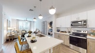 This thoughtfully designed single-floor residence offers a cohesive blend of modern aesthetics and functional living. The open-concept kitchen is a standout feature, showcasing a large center island with a white quartz countertop and undermount sink, two-tone cabinetry pairing white uppers with warm wood-finish lowers, a classic subway tile backsplash, and a full suite of stainless steel appliances. Globe pendant lights hang above the island, adding a stylish focal point to the space.

The adjoining living area is bright and welcoming, with large windows dressed in sheer curtains that invite natural light and offer views of lush outdoor greenery. Light wood-style flooring runs throughout the main living areas, complementing the warm, neutral palette.

Each bedroom features plush carpet, a ceiling fan, and windows with views of palm-lined surroundings. The primary bedroom is served by an en-suite bathroom complete with a glass-enclosed walk-in shower, wood-tone vanity with quartz countertop, and convenient access to a stacked in-unit washer and dryer. A second full bathroom mirrors the same refined finishes, including a large vanity mirror and wood-finish cabinetry. The overall ambiance is clean, contemporary, and move-in ready.